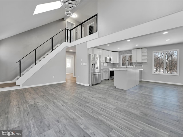 unfurnished living room featuring stairs, light wood finished floors, a skylight, and baseboards