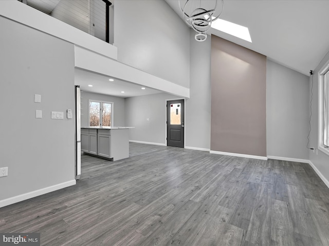 unfurnished living room featuring dark wood-style floors, high vaulted ceiling, a skylight, and baseboards