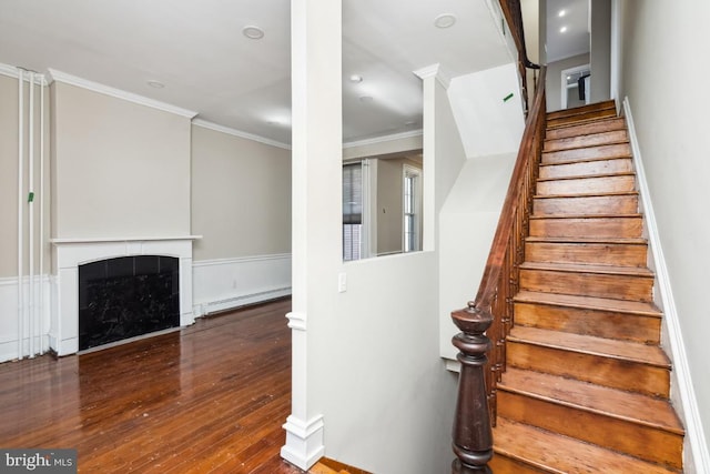 staircase featuring a baseboard heating unit, a fireplace, wood-type flooring, and crown molding