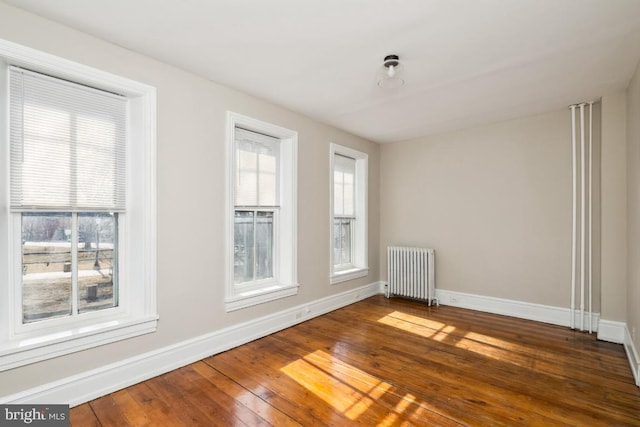 unfurnished room with baseboards, a healthy amount of sunlight, hardwood / wood-style floors, and radiator heating unit