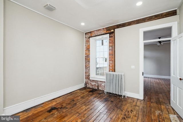 spare room featuring radiator, visible vents, brick wall, baseboards, and hardwood / wood-style flooring