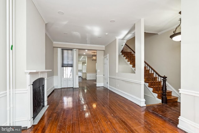 unfurnished living room featuring stairs, ornamental molding, a fireplace, and hardwood / wood-style flooring