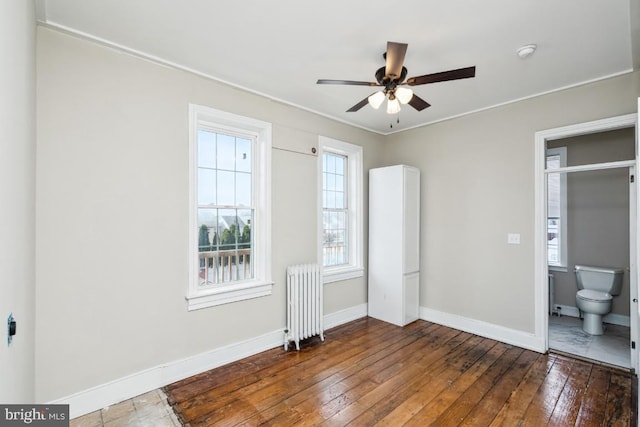 unfurnished bedroom featuring radiator, connected bathroom, baseboards, and hardwood / wood-style flooring