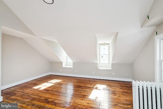 additional living space featuring lofted ceiling, radiator, baseboards, and hardwood / wood-style flooring