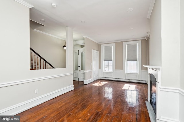 unfurnished living room with hardwood / wood-style floors, baseboard heating, crown molding, and wainscoting