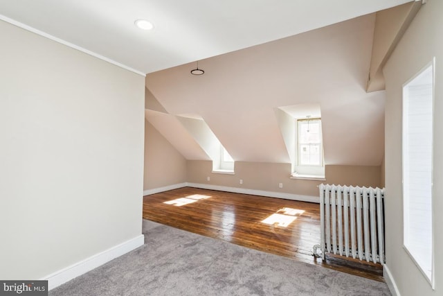 additional living space featuring vaulted ceiling, radiator heating unit, wood finished floors, and baseboards