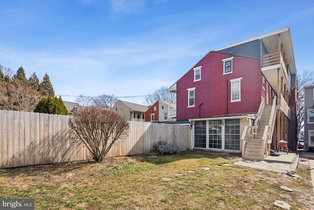 back of house featuring a fenced backyard, brick siding, a sunroom, stairs, and a yard