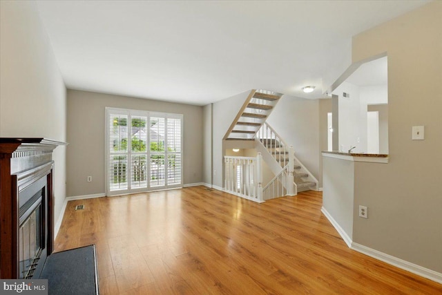 10204 Faire Commons Ct, Burke, VA 22015 - unfurnished living room featuring light wood-style flooring, a glass covered fireplace, baseboards, and stairway