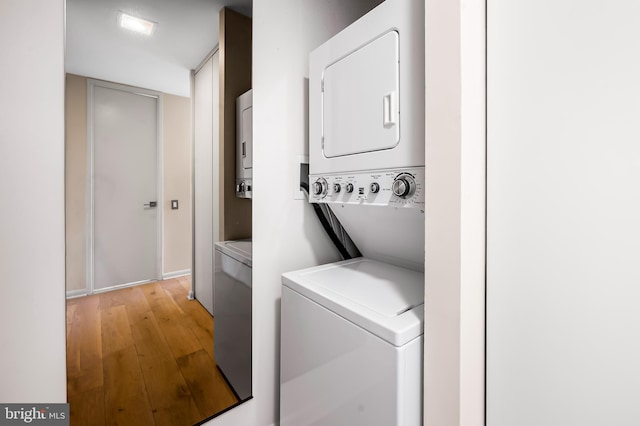 clothes washing area with laundry area, stacked washer and clothes dryer, and light wood-type flooring