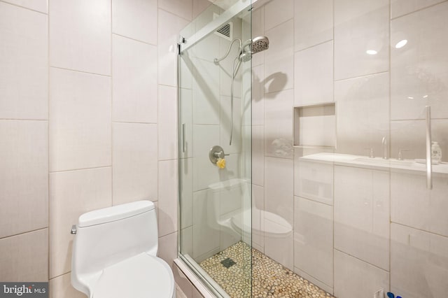 bathroom featuring toilet, tile walls, and a shower stall