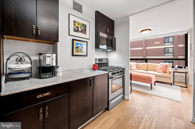 kitchen featuring visible vents, light wood-style flooring, stainless steel appliances, dark brown cabinetry, and light stone countertops