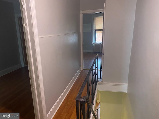 corridor with baseboards, wood finished floors, and an upstairs landing