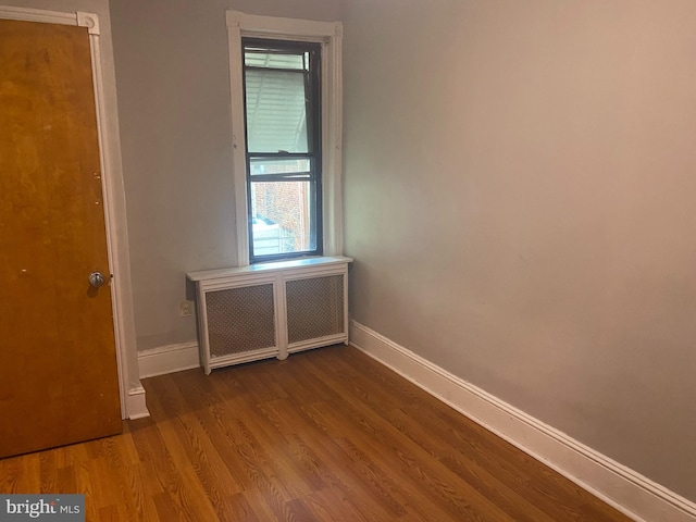 empty room with baseboards, dark wood-type flooring, and radiator