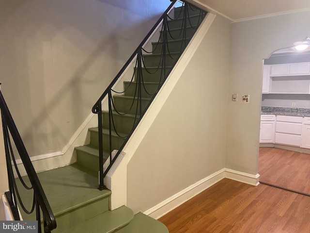 staircase with ornamental molding, wood finished floors, and baseboards