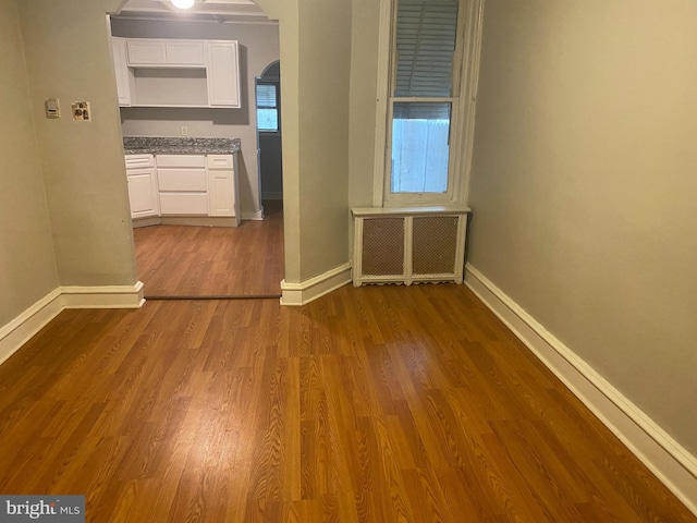 spare room with arched walkways, baseboards, wood finished floors, and radiator