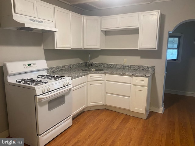 kitchen featuring arched walkways, white cabinets, a sink, white range with gas stovetop, and under cabinet range hood