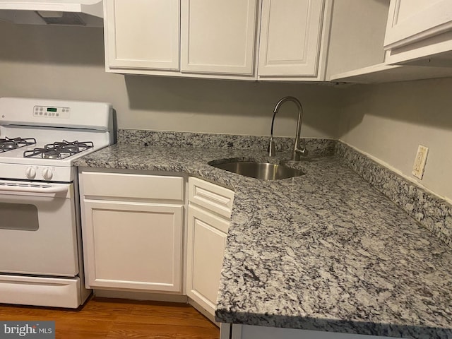 kitchen featuring under cabinet range hood, white range with gas stovetop, a sink, white cabinetry, and light wood finished floors