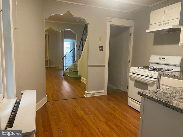 kitchen with under cabinet range hood, wood finished floors, white cabinetry, baseboards, and white range with gas cooktop