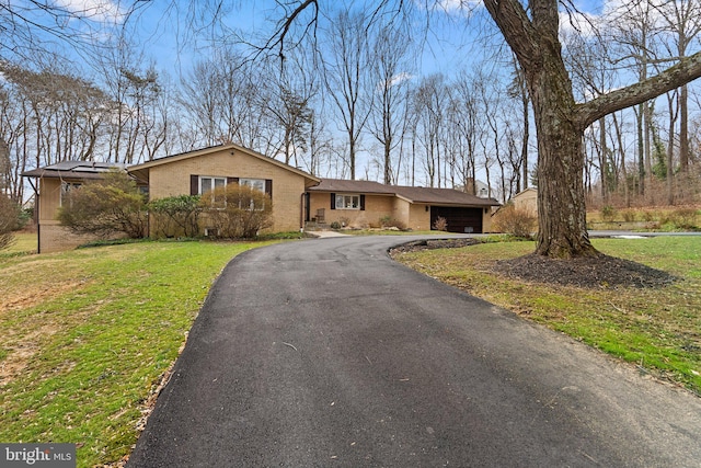 view of front of home with driveway, a chimney, a front lawn, a garage, and brick siding