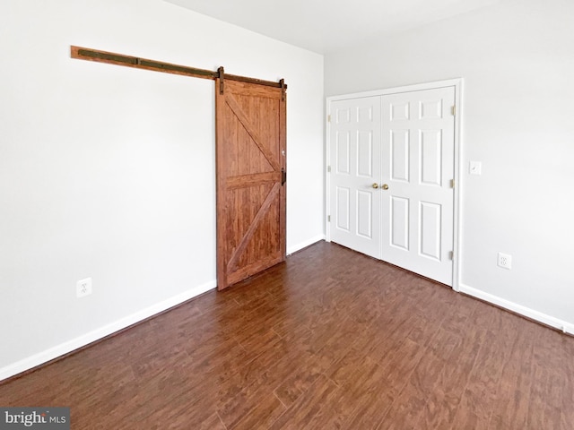 unfurnished bedroom with a barn door, baseboards, and dark wood-style flooring