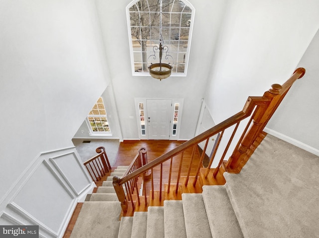 stairs with wood finished floors, a towering ceiling, and baseboards