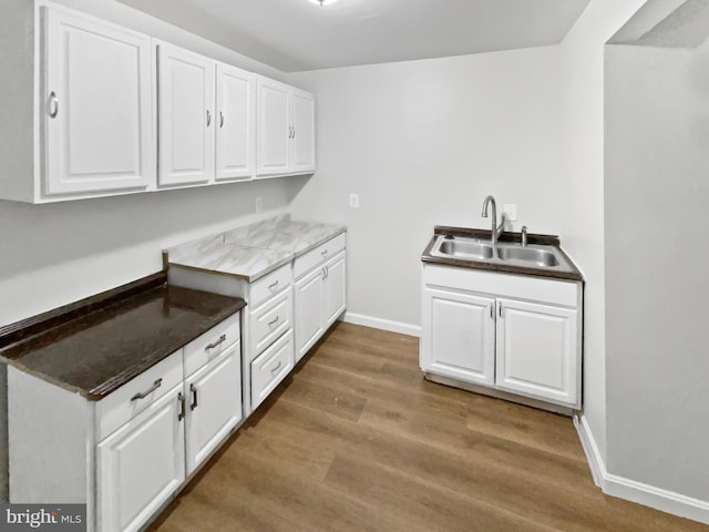 kitchen with baseboards, wood finished floors, a sink, and white cabinets