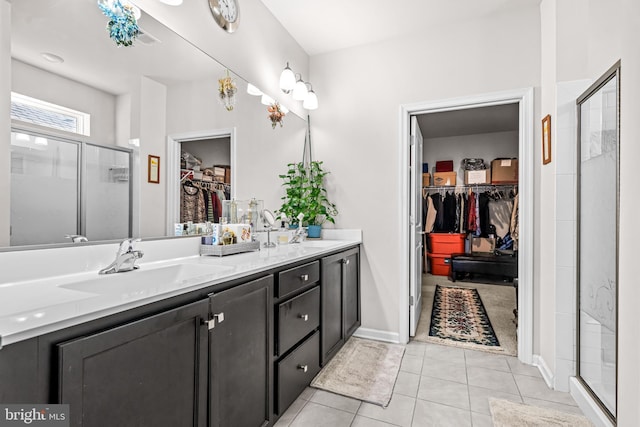 bathroom with a walk in closet, double vanity, a stall shower, a sink, and tile patterned floors