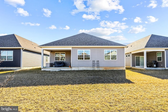 rear view of property featuring roof with shingles, a patio area, and a lawn