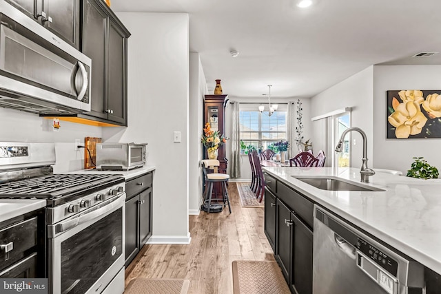 kitchen featuring a notable chandelier, stainless steel appliances, a sink, baseboards, and light wood finished floors