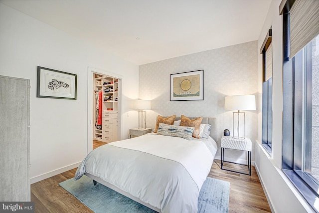 bedroom with wallpapered walls, baseboards, wood finished floors, a spacious closet, and a closet