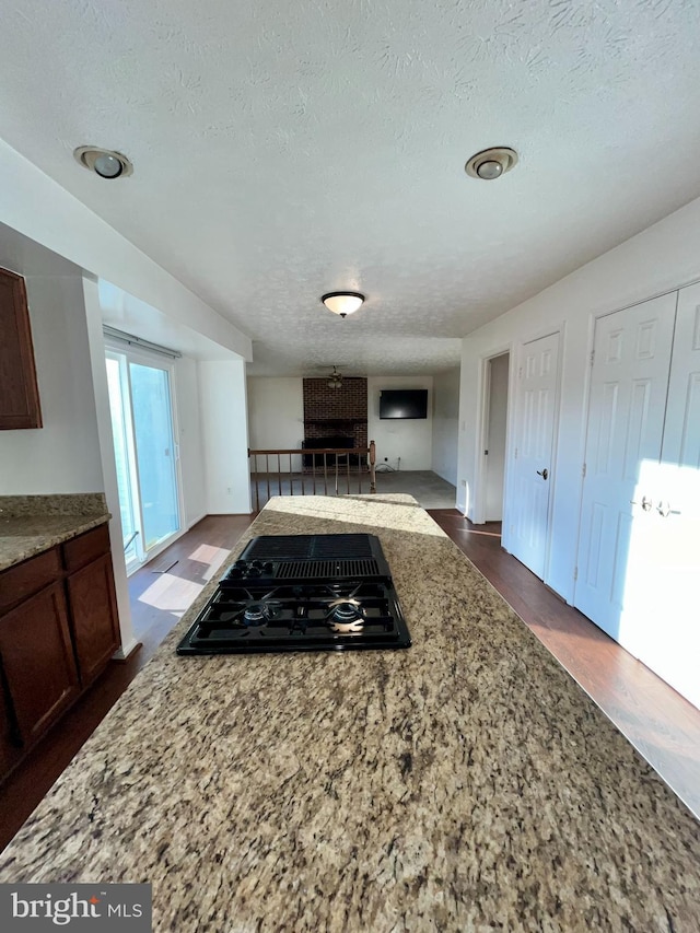 kitchen with light stone counters, dark wood finished floors, open floor plan, a textured ceiling, and black gas stovetop