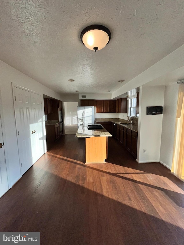 kitchen featuring dark wood finished floors, a center island, a textured ceiling, white fridge with ice dispenser, and a sink