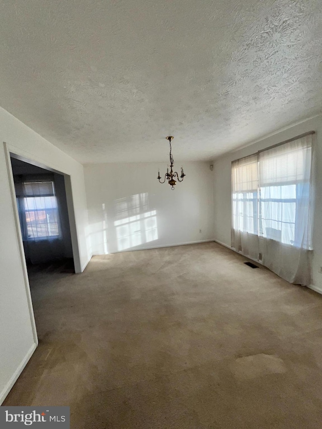 empty room featuring a notable chandelier, a textured ceiling, visible vents, and carpet flooring