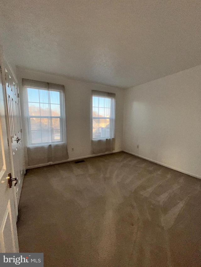 empty room with a textured ceiling, carpet, visible vents, and baseboards