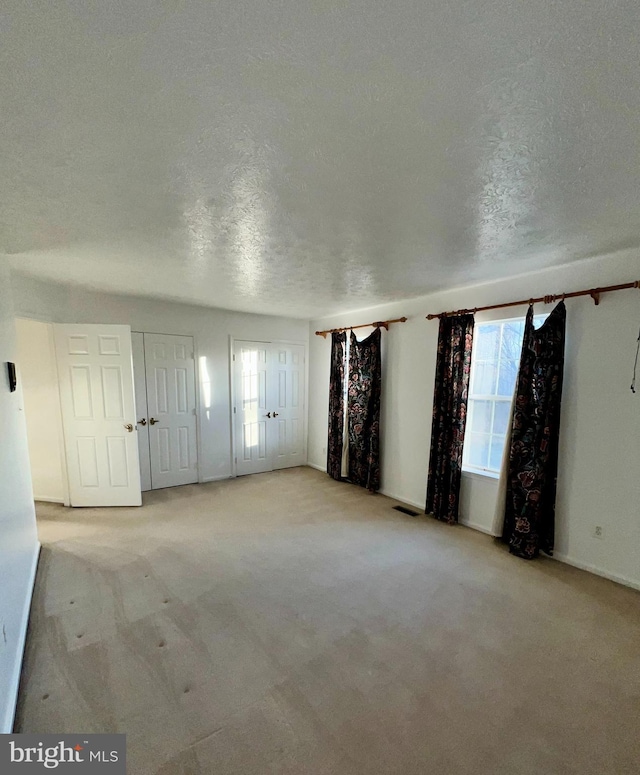 unfurnished room featuring carpet, visible vents, a healthy amount of sunlight, and a textured ceiling