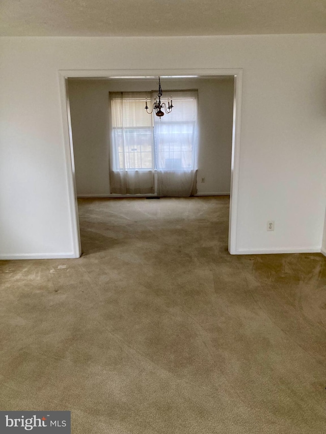 unfurnished dining area featuring a notable chandelier, carpet floors, and baseboards