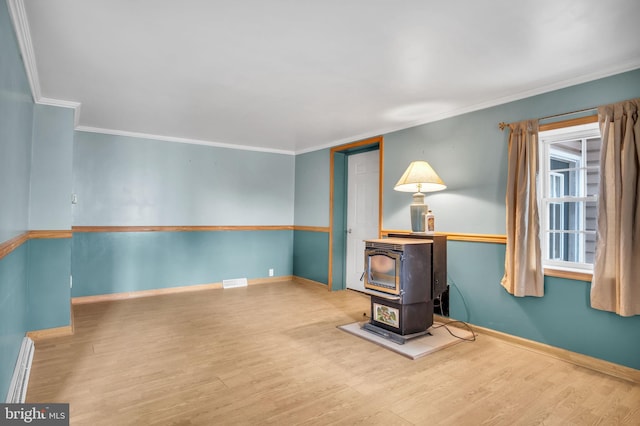 interior space featuring ornamental molding, wood finished floors, a wood stove, and baseboards