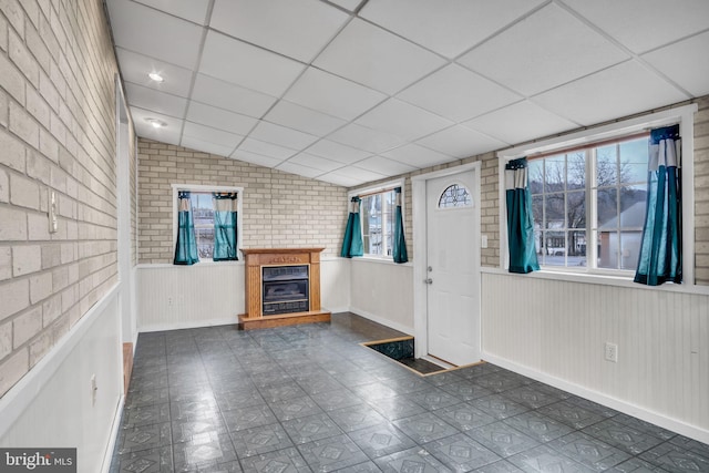 entrance foyer with lofted ceiling, brick wall, a drop ceiling, and a glass covered fireplace