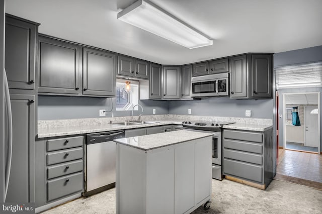 kitchen with a kitchen island, light stone countertops, stainless steel appliances, gray cabinetry, and a sink