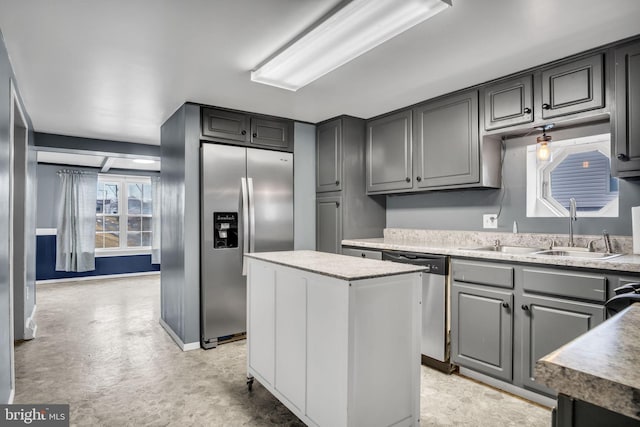 kitchen featuring appliances with stainless steel finishes, a center island, light countertops, gray cabinetry, and a sink