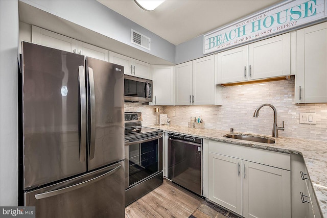 kitchen with visible vents, backsplash, appliances with stainless steel finishes, a sink, and light stone countertops