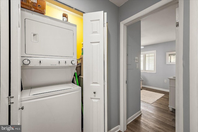 clothes washing area featuring stacked washer / dryer, laundry area, baseboards, and wood finished floors