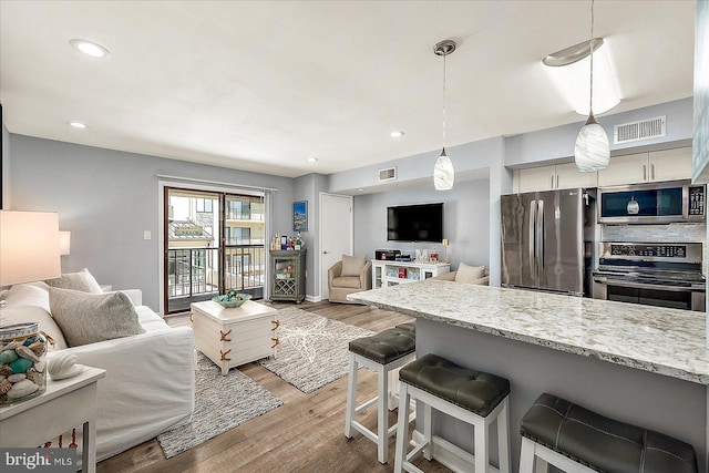 kitchen with stainless steel appliances, visible vents, open floor plan, light wood-type flooring, and a kitchen bar