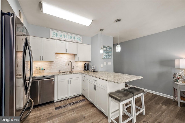 kitchen featuring stainless steel dishwasher, freestanding refrigerator, white cabinets, a sink, and a peninsula