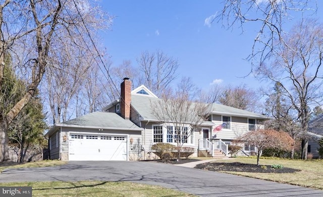 split level home with a garage, a chimney, and driveway