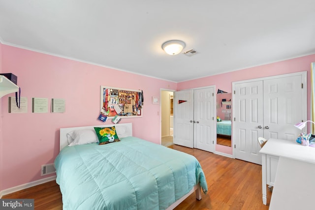 bedroom featuring light wood-style flooring, baseboards, visible vents, and two closets