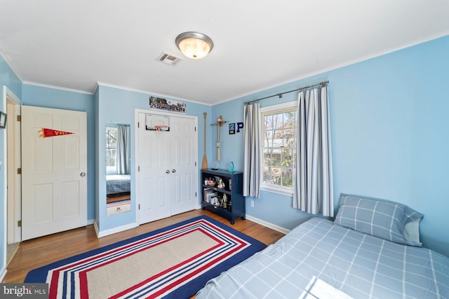 bedroom with visible vents, ornamental molding, wood finished floors, a closet, and baseboards