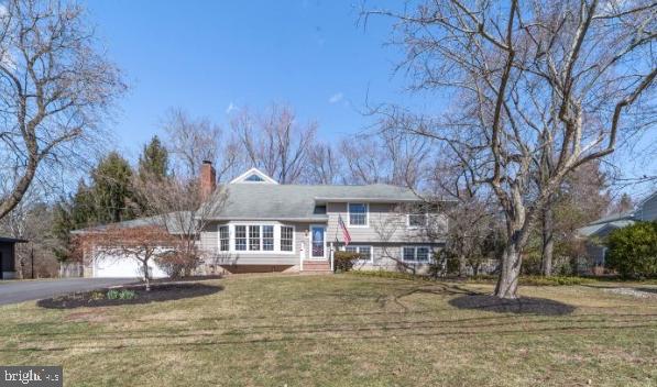 tri-level home featuring aphalt driveway, an attached garage, a chimney, and a front yard