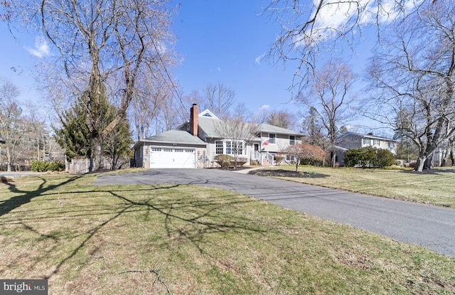 view of front of house featuring aphalt driveway, an attached garage, a front yard, and a chimney