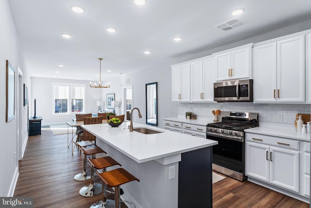 kitchen with dark wood-type flooring, a sink, visible vents, appliances with stainless steel finishes, and tasteful backsplash